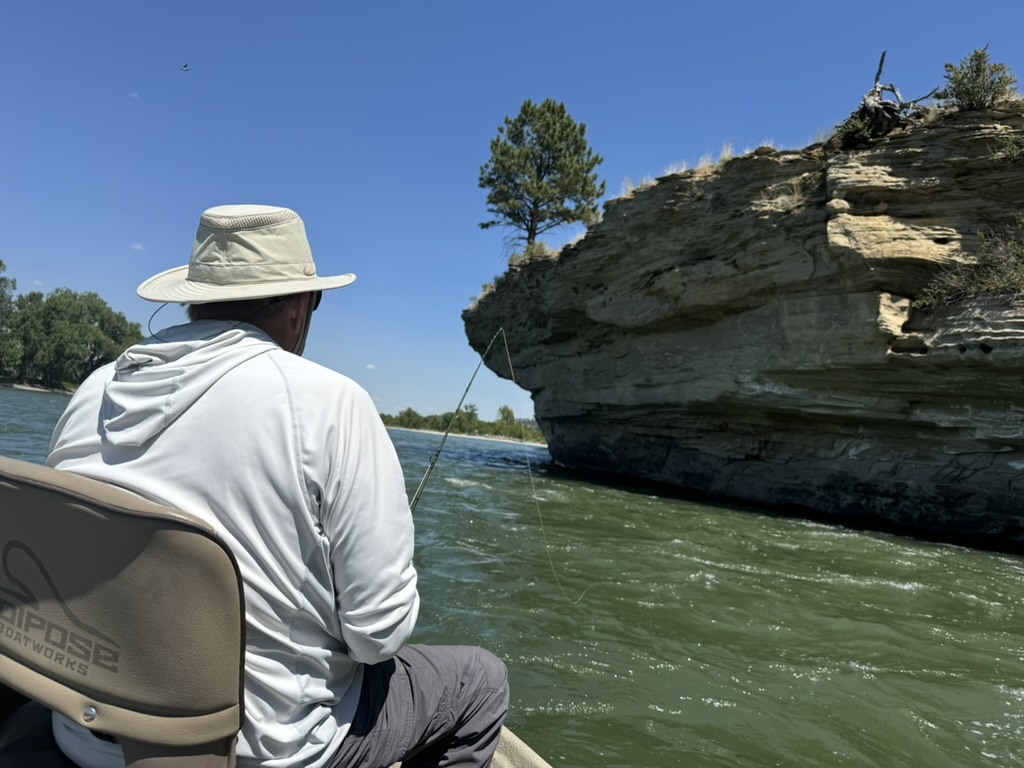 Angler casting from drift boat near rock cliffs