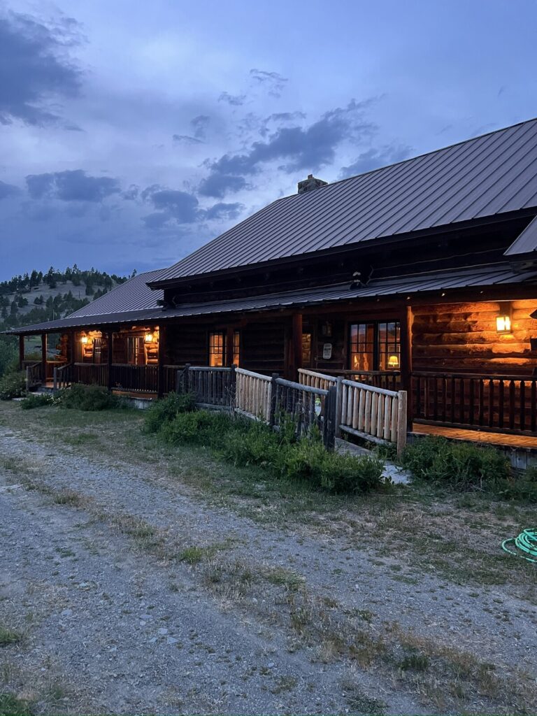 Spring Creek Lodge log exterior at dusk with warm-lit windows and wraparound porch
