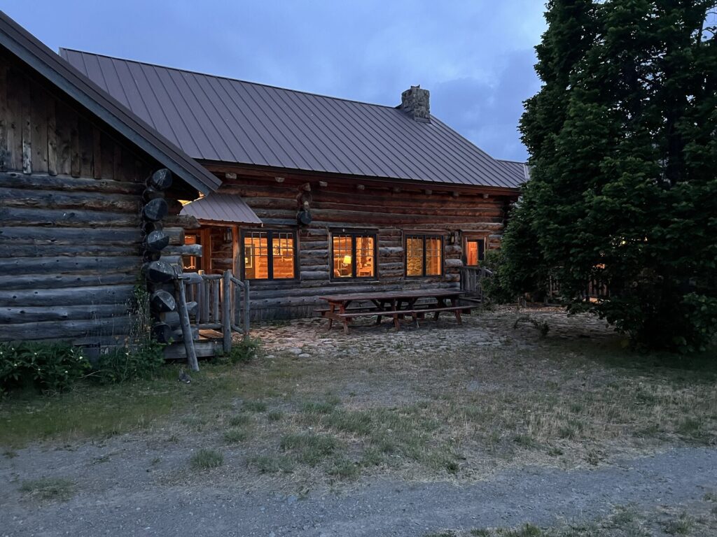 Spring Creek Lodge log gable end at dusk with a picnic table and glowing windows