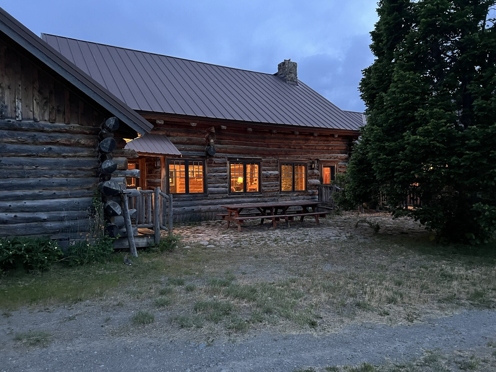 Spring Creek Lodge log gable end at dusk with a picnic table and glowing windows
