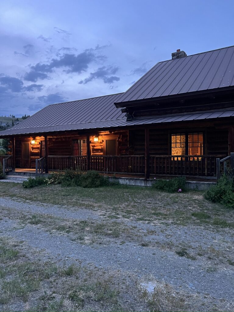 Spring Creek Lodge covered porch glowing at dusk along the log facade