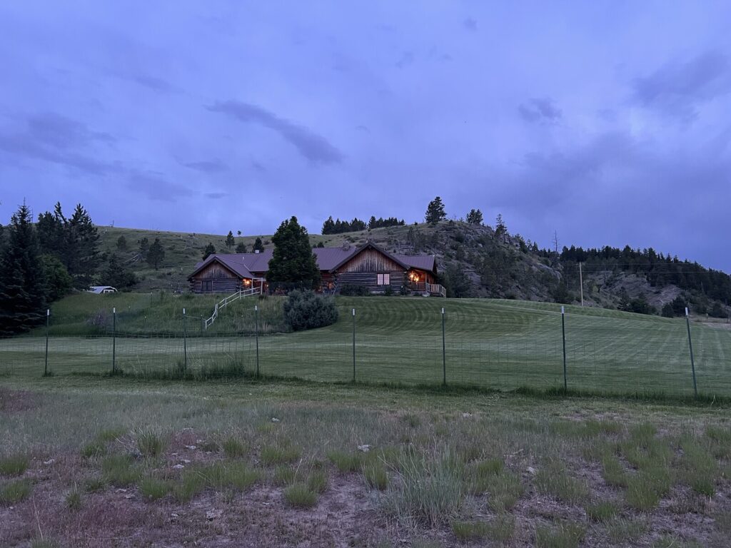 Spring Creek Lodge nestled on a pine and rimrock hillside above an open meadow at dusk