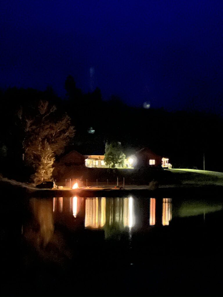 Spring Creek Lodge lit at night reflected across the pond beside a streamside fire