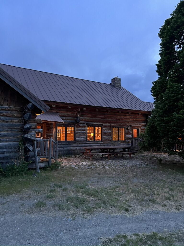 Spring Creek Lodge log gable end and picnic table beneath a tall tree at dusk