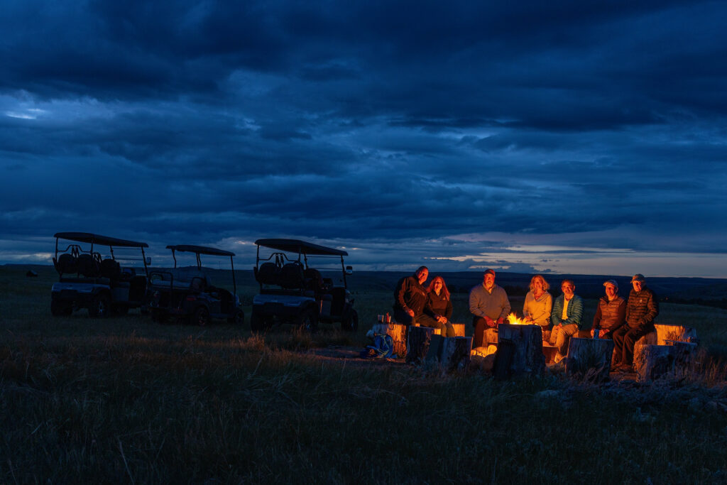 Guests gathered around the hilltop firepit at dusk with golf carts parked on the ridge